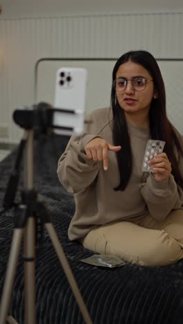 A-happy-confident-brunette-girl-in-glasses-blogs-about-medicine-tablets-and-capsules-using-her-white-smartphone-in-a-modern-apartment-at-home